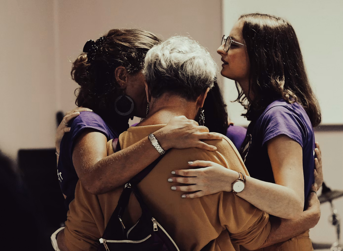 Three women embracing in a warm, supportive group hug